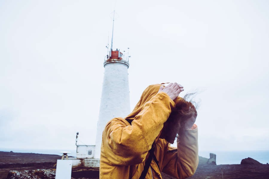 man trying to protect himself from the strong wind in Iceland covering his head with his hoodie