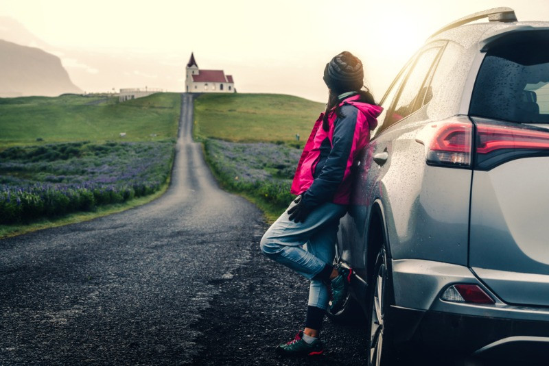 Girl with a rental car in Iceland looking at the views leaning on her car