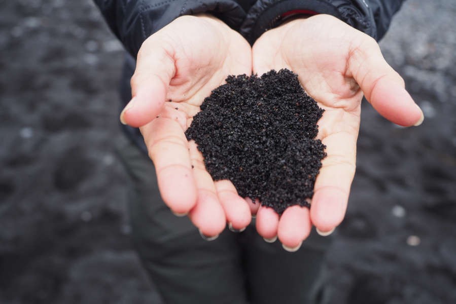 girl holding some black sand it is usually carries away in Sandstorms in Iceland