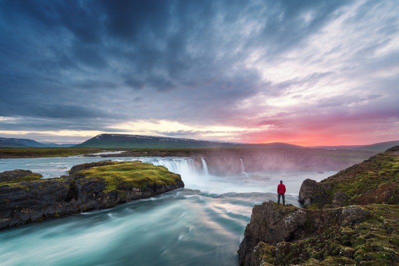Visitor overlooking some waterfalls with the midnight sun in the background - Is Iceland worth visiting