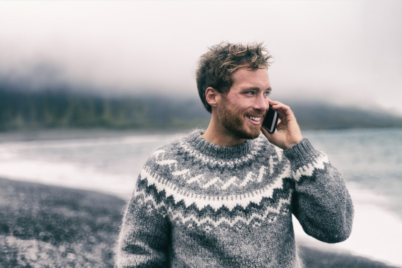 young man using a sim card for Iceland travels making a call by the ocean