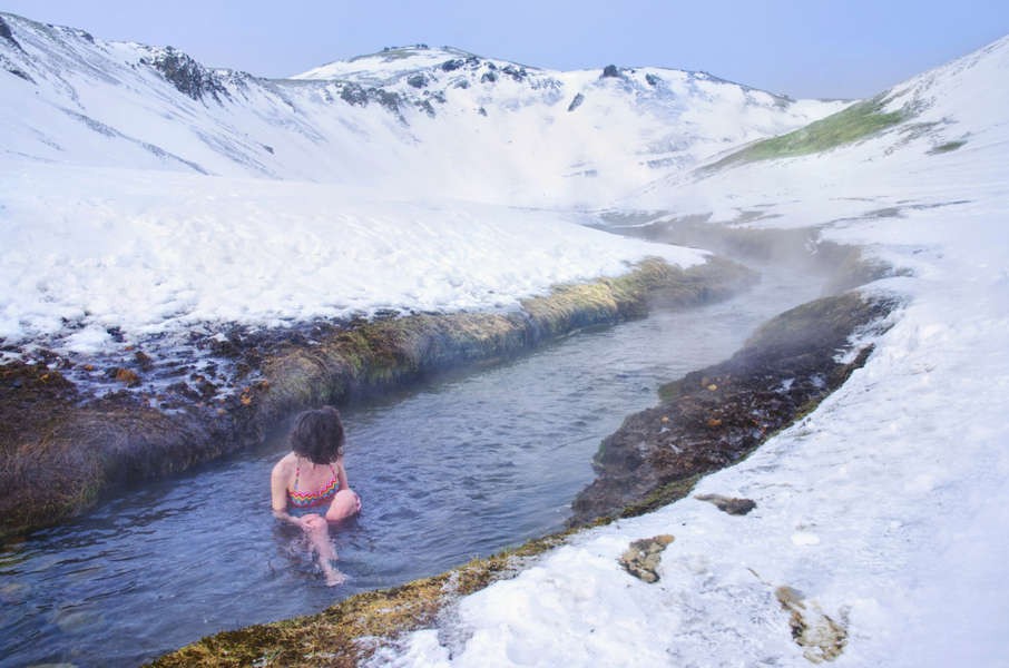 woman bathing in reykjadalur hot river with snowy mountains