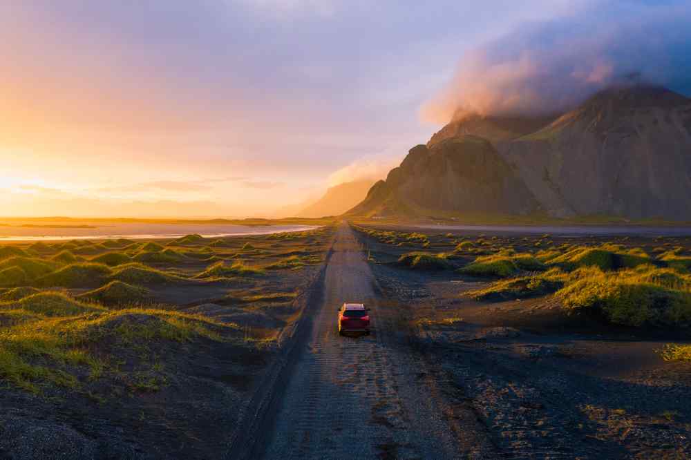 Iceland's South Coast Car driving along Iceland’s South Coast at sunset with mountains and black sand scenery.