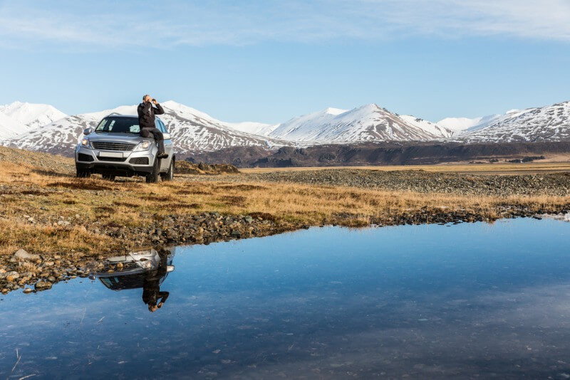 Men seating on his rental car in icelandic landscape