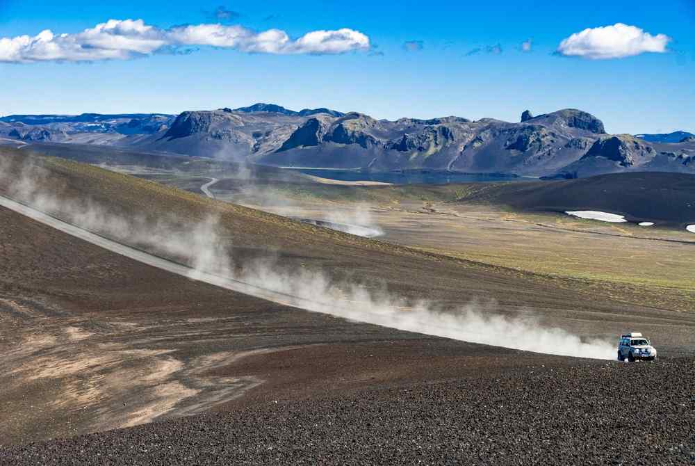 Iceland's Highlands 4x4 vehicle driving across a dusty gravel road in the Icelandic Highlands with mountains in the background.