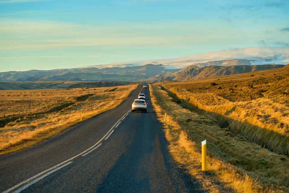 Ring Road during summer Cars driving along a paved Icelandic road at sunset with open landscapes on both sides.