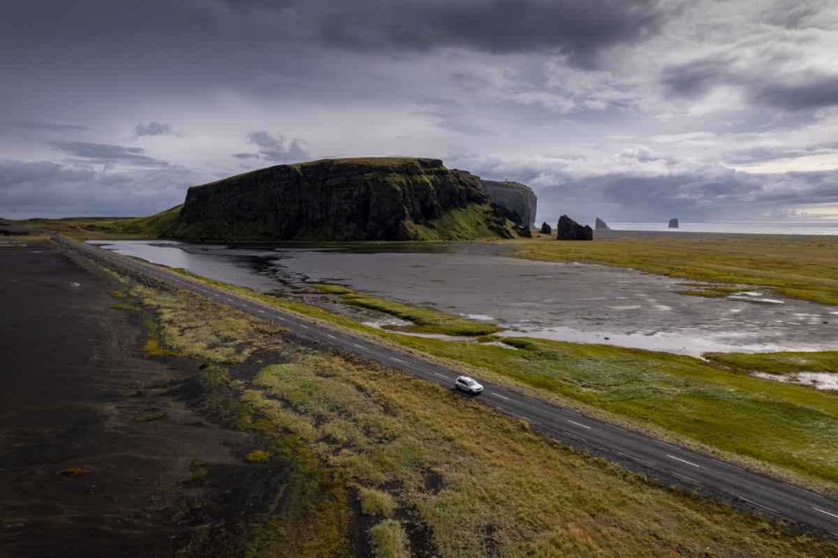 White vehicle driving by a remote black beach in Iceland