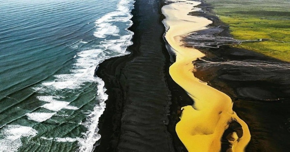 Unusual yellow river in Iceland in contrast with the black sand beach and a green moss field