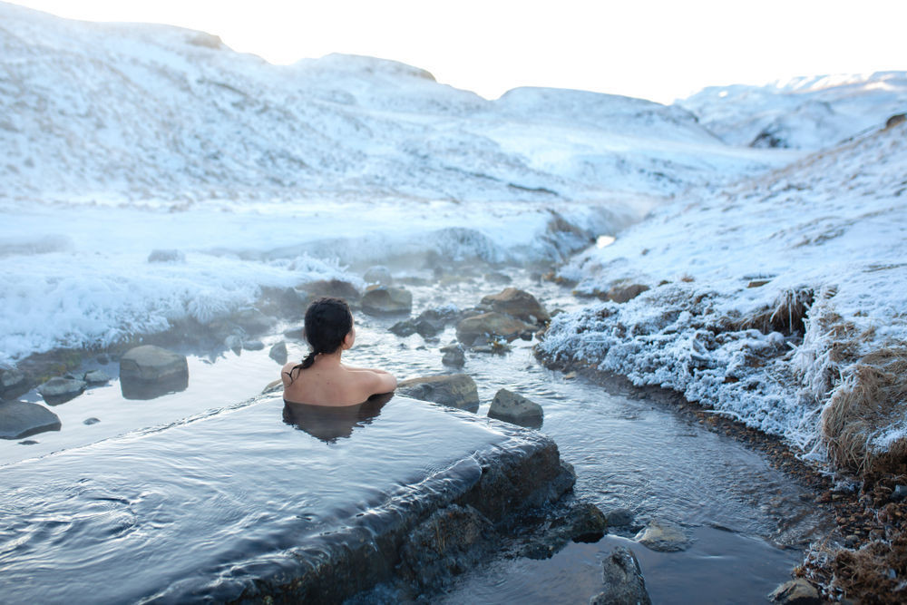 Girl bathing in geothermal waters surrounded by a snowy mountains in winter