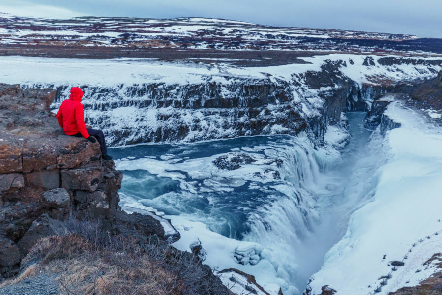 Boy sitting on the edge of a cliff of Gulfoss waterfall in winter