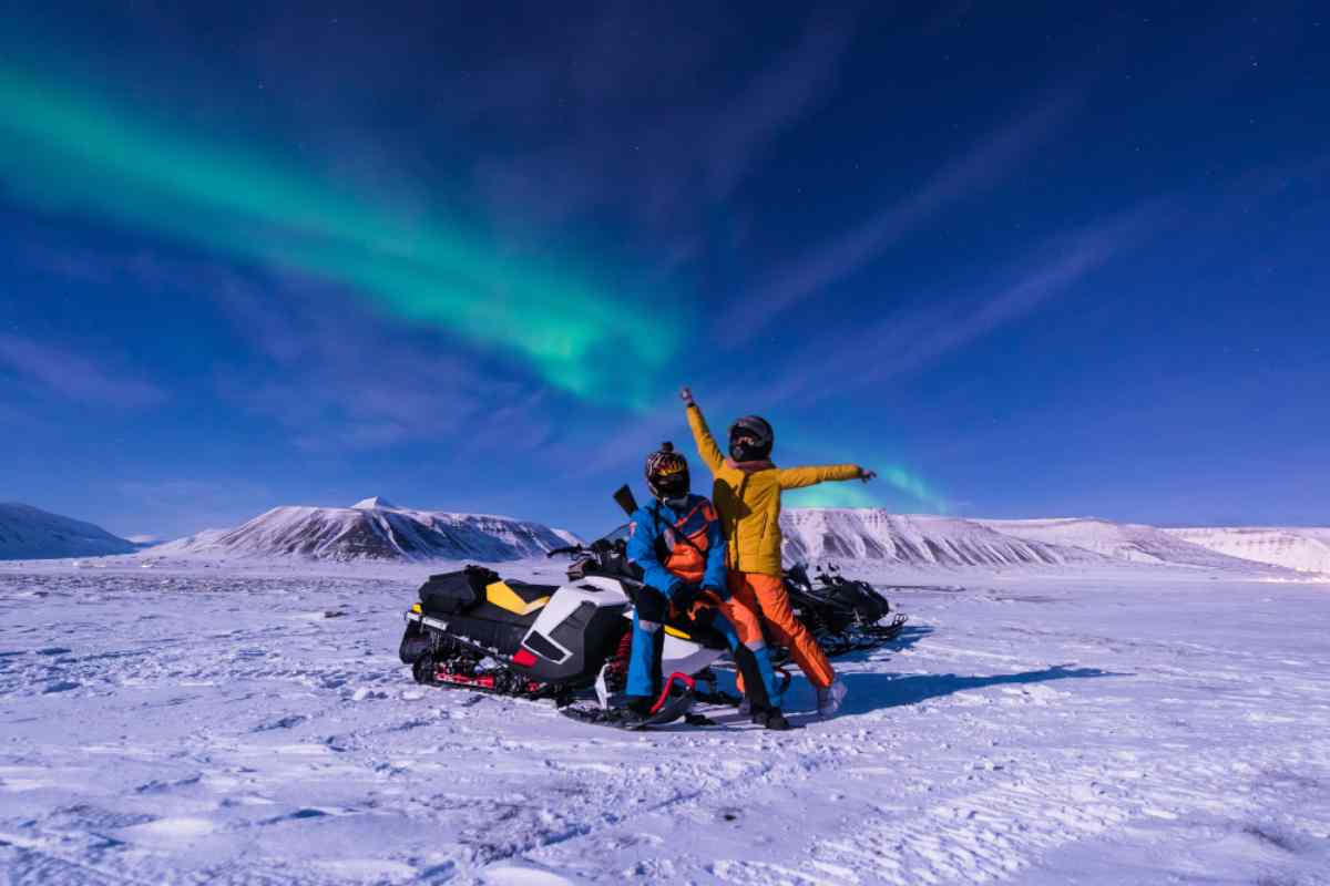 Northern lights over two tourists practising snowmobiling