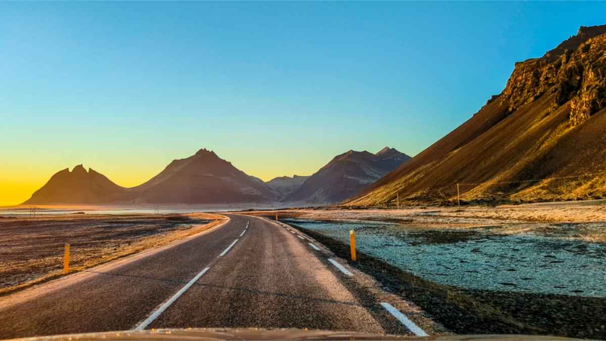 Sun setting in the horizon of a road in Iceland with mountains at the back