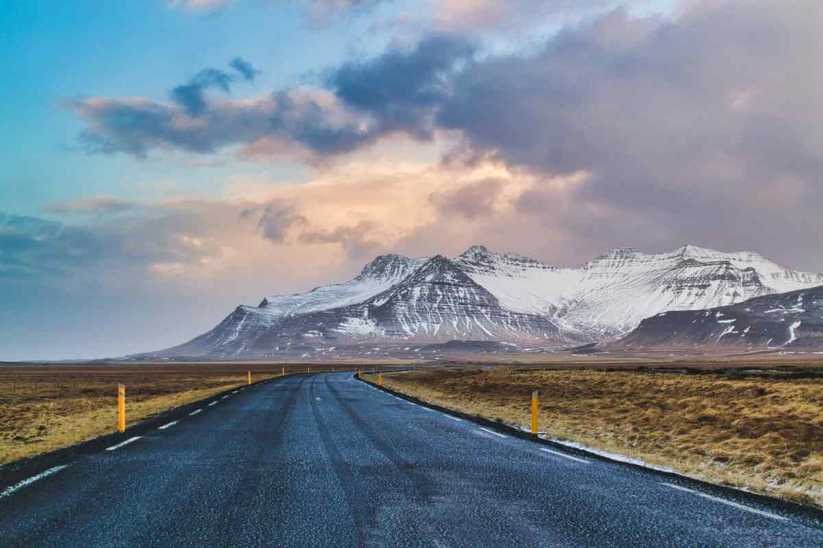 Open road in Iceland leading to snow-capped mountains under a colorful winter sky.