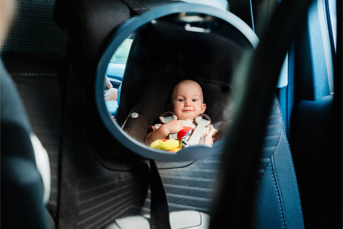 Wann ist es in Island verpflichtend, einen Kindersitz oder eine Sitzerhöhung zu verwenden? Baby lächelt durch einen Spiegel, während es in seinem Kindersitz angeschnallt ist