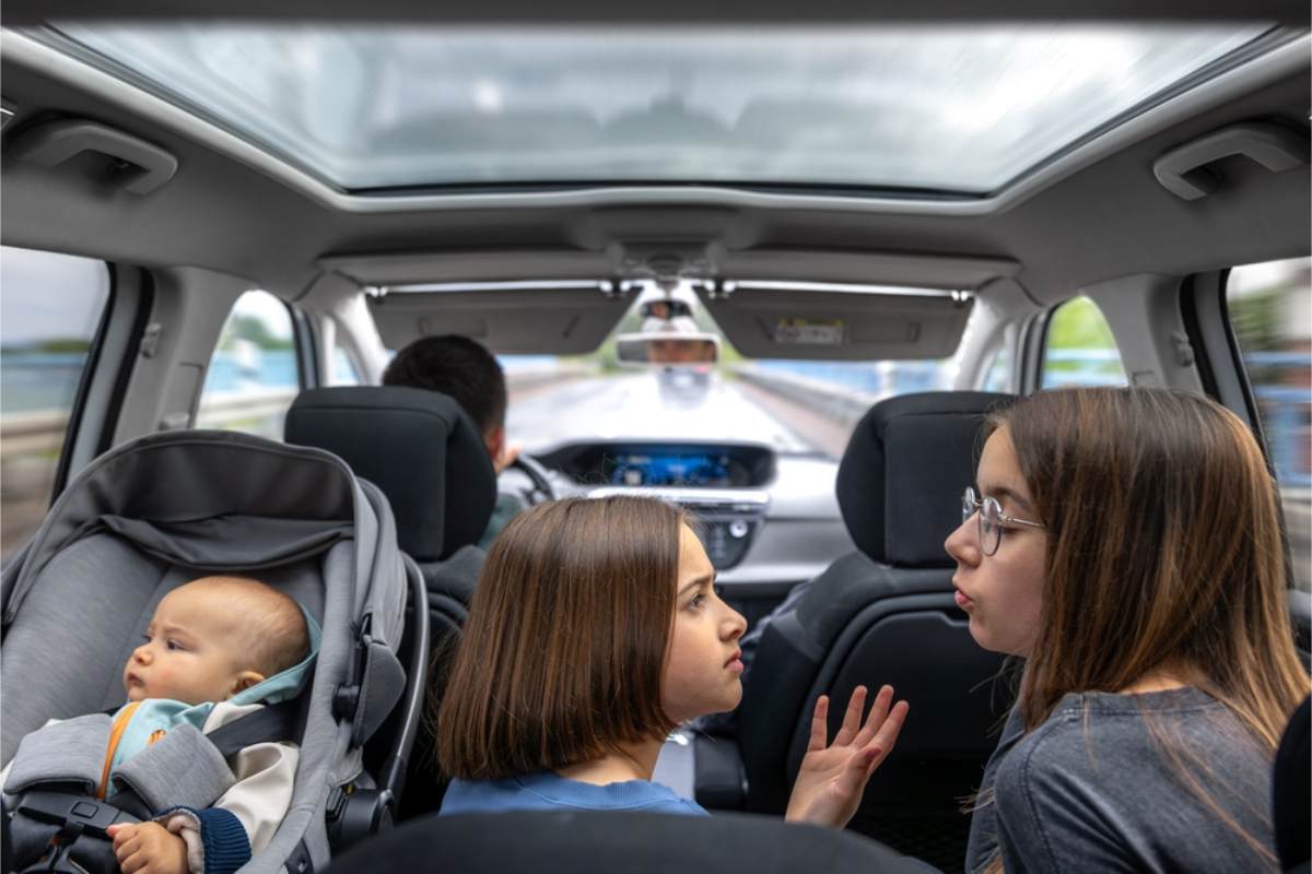 Was sagen die Vorschriften zu aktiven Airbags und Kindern auf dem Vordersitz? Mehrere Kinder sitzen mit ihren jeweiligen Sitzen in einem Mietwagen