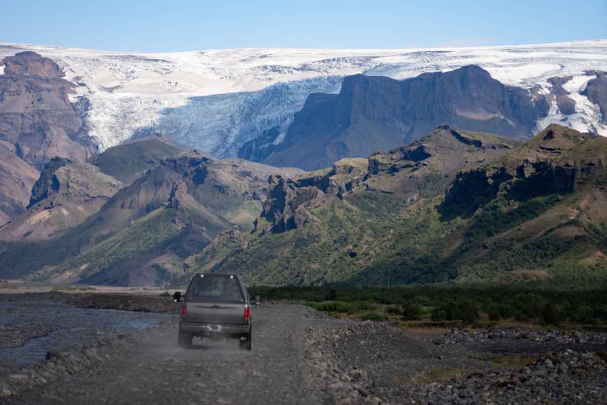 Ein 4x4 f&auml;hrt &uuml;ber die isl&auml;ndischen Stra&szlig;en, w&auml;hrend in der Ferne einige der imposanten felsigen Ebenen der Insel zu sehen sind.