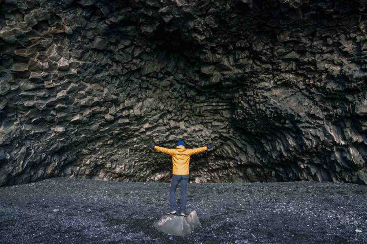 Tourist steht in der Bucht des schwarzen Strandes Reynisfjara mit einer knallgelben Jacke