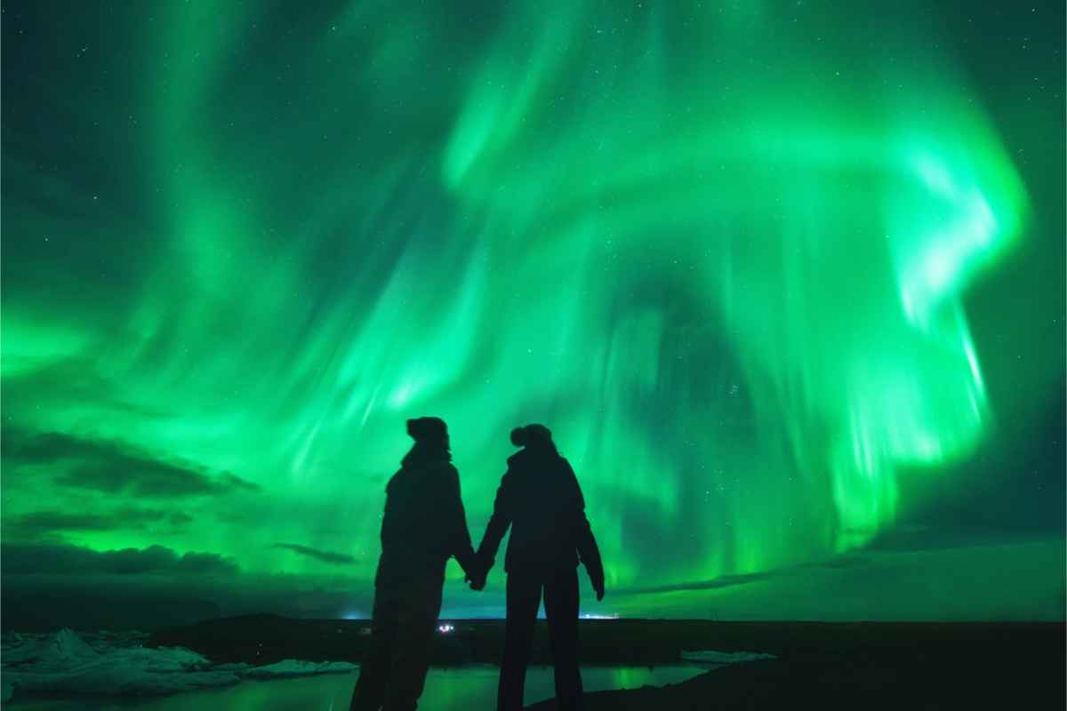 Paar beobachtet die Nordlichter am Himmel, während es sich an den Händen hält