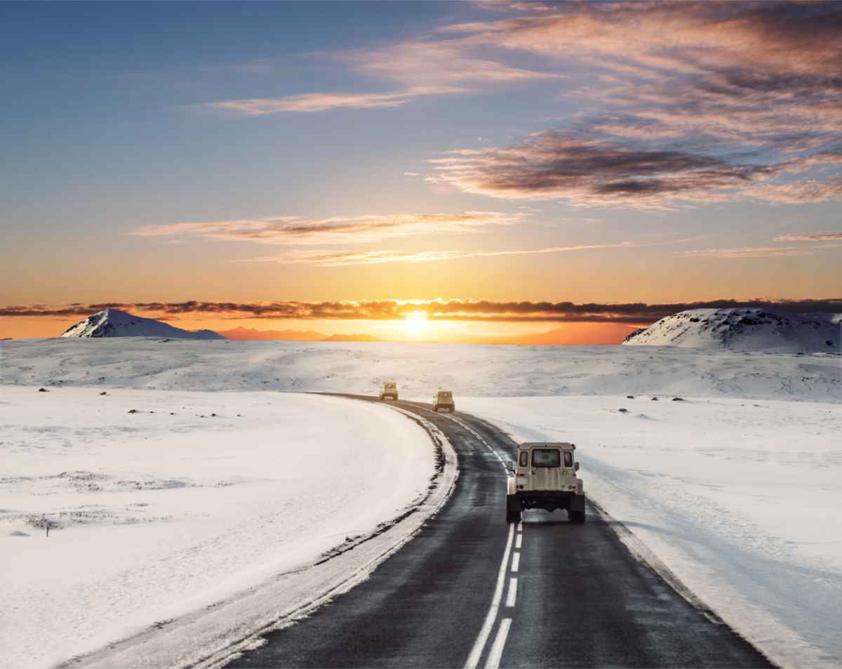 Sommer vs. Winter in Island Mehrere Jeeps auf Islands Ring Road mit schneebedeckter Landschaft in der Dämmerung