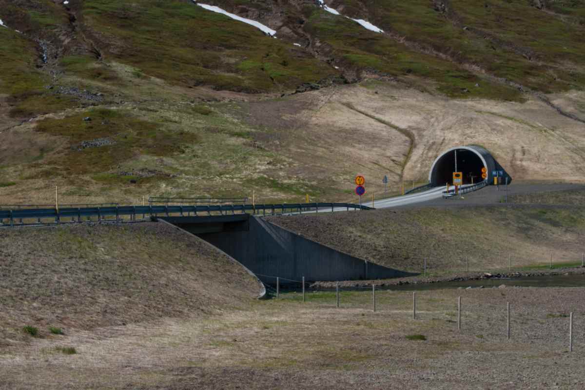 Túnel Héðinsfjarðargöng en Islandia Entrada de un túnel en una zona rural de Islandia con laderas cubiertas de hierba y restos de nieve