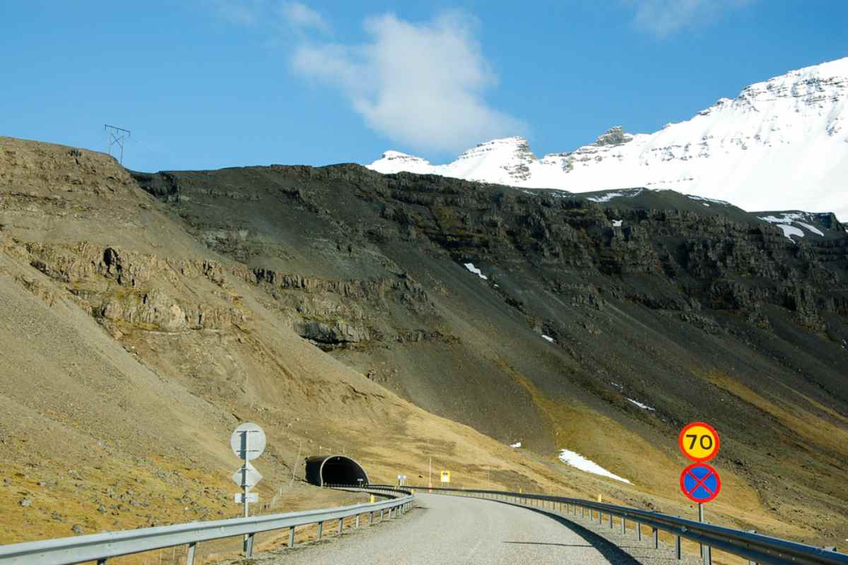 Límites de velocidad en los túneles de Islandia Carretera que conduce a un túnel de montaña en Islandia con señales de límite de velocidad y picos nevados arriba