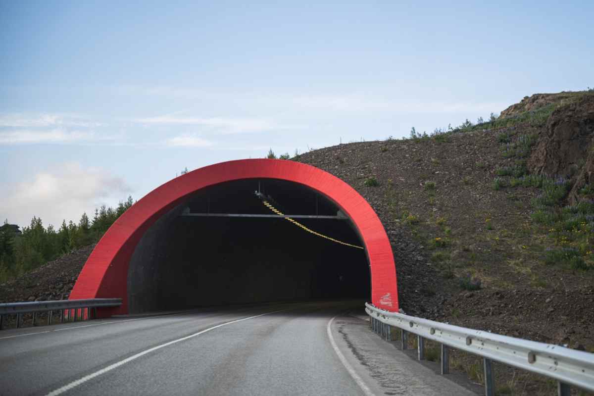 Lo que debes saber sobre los túneles de peaje en Islandia Entrada roja de un túnel en una carretera asfaltada en Islandia rodeada de terreno rocoso