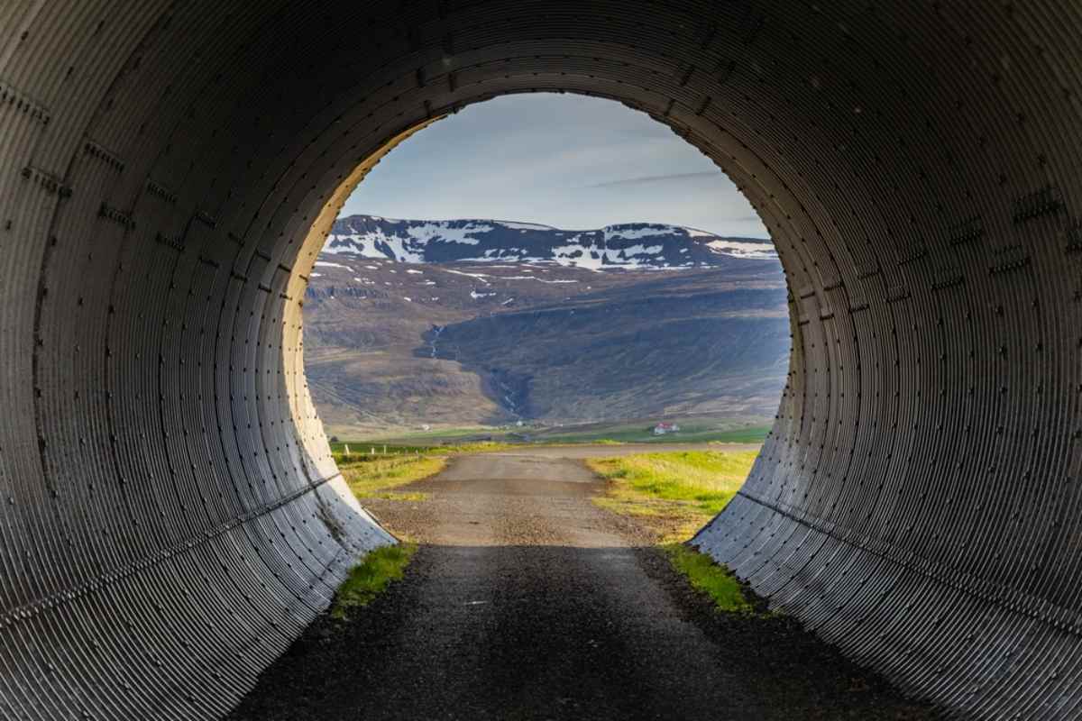 Planificar un viaje por carretera por Islandia con túneles Vista a través de un túnel redondo en Islandia hacia un valle con montañas al fondo