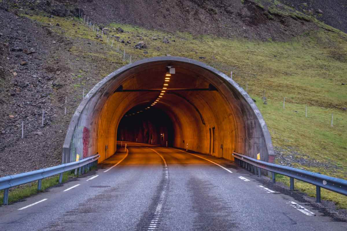 La importancia de los túneles en Islandia Entrada iluminada de un túnel de carretera en Islandia situada en una empinada ladera verde y rocosa