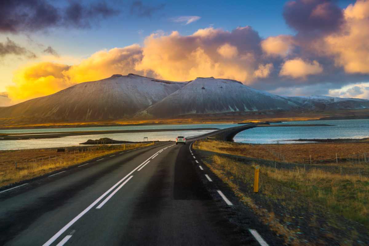 Coche blanco saliendo a toda velocidad por la circunvalación de Islandia al atardecer