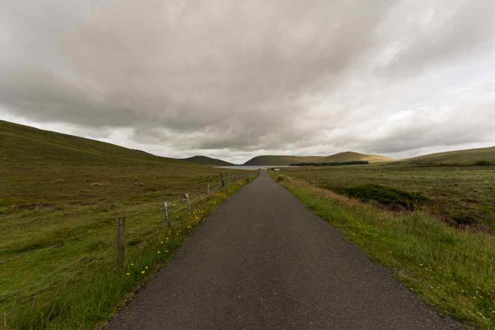 Carretera rural en Islandia Carretera rural estrecha a través de colinas verdes islandesas bajo un cielo nublado.