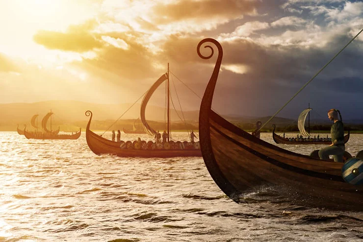 Varios barcos vikingos navegando al atardecer, con guerreros a bordo, velas desplegadas y un cielo dramático en el fondo