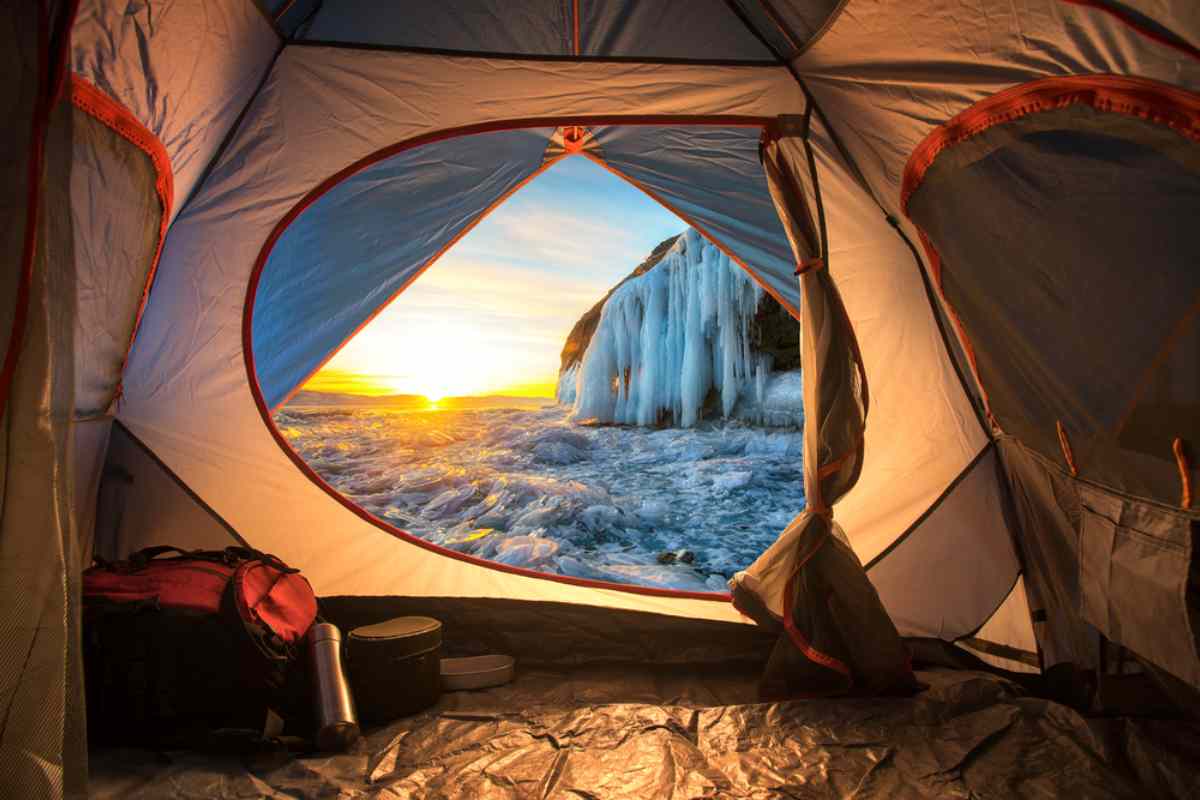 Vista desde el interior de una tienda de campaña al amanecer, con vistas a un paisaje helado con formaciones de hielo y un horizonte brillante, capturando la serena belleza del campamento invernal.