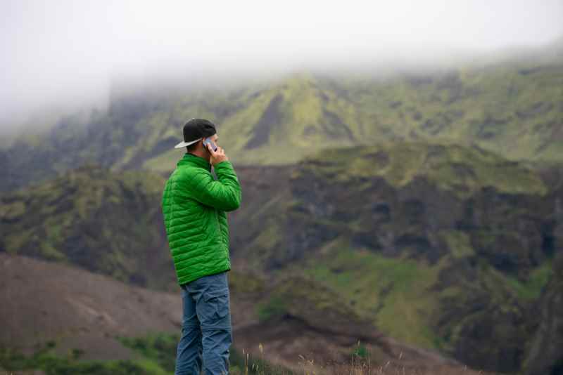 Hombre con chaqueta verde hablando por tel&eacute;fono en un paisaje monta&ntilde;oso y brumoso de Islandia.