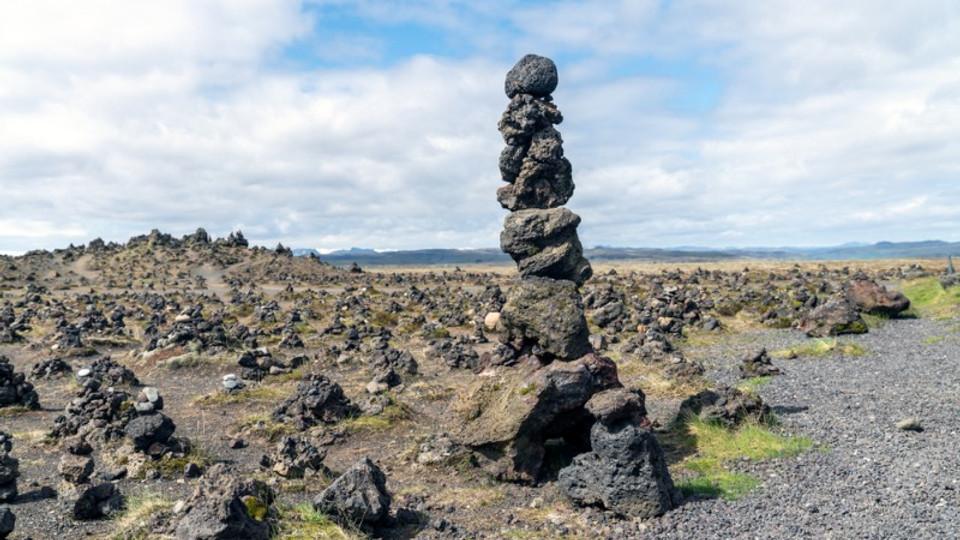Gran pila de rocas volcánicas en un campo de cairns de piedra bajo un cielo azul brillante, representando el paisaje y las tradiciones únicas de Islandia.