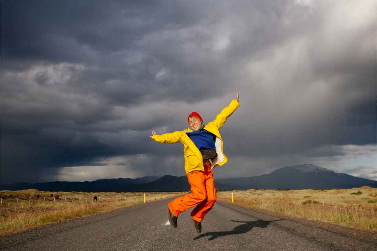 Ropa impermeable y cortaviento para Islandia Turista alegre en Islandia saltando en medio de la carretera con la ropa adecuada para este tiempo
