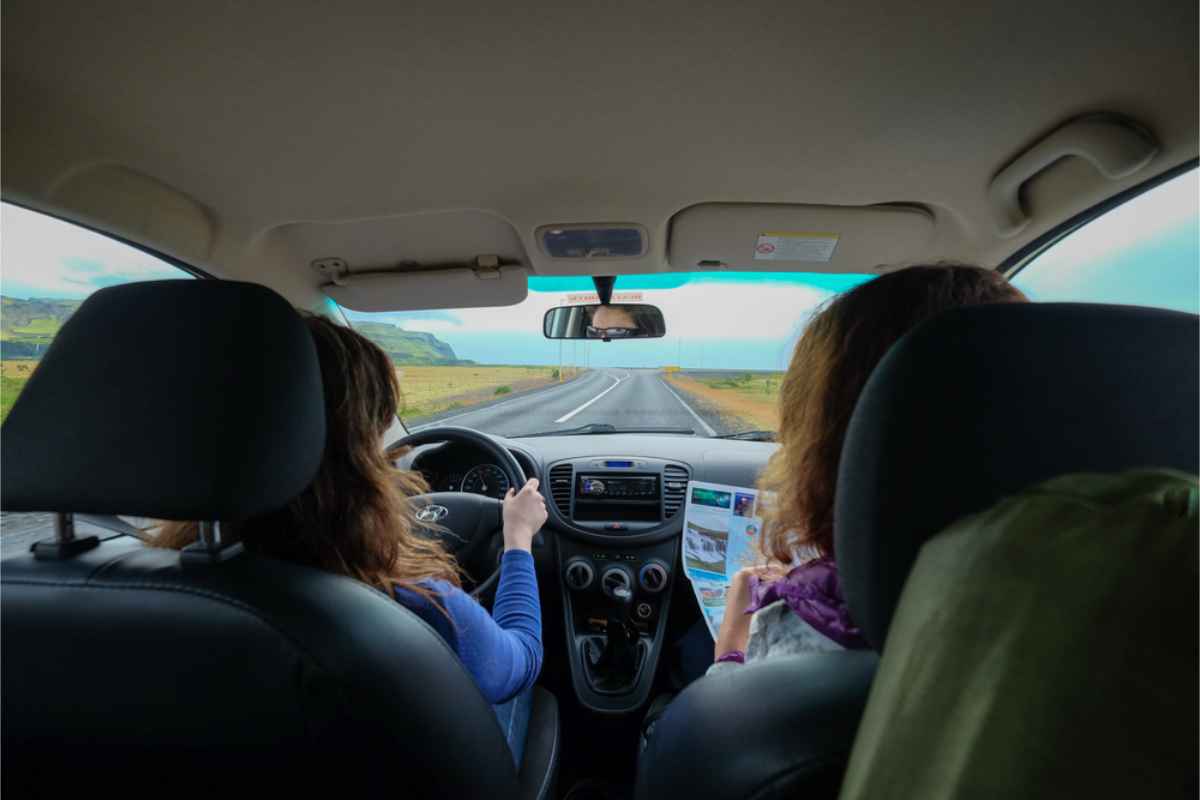 Qué llevar dentro de tu coche de alquiler Dos mujeres conduciendo un coche en Islandia, la copiloto sostiene un mapa de papel