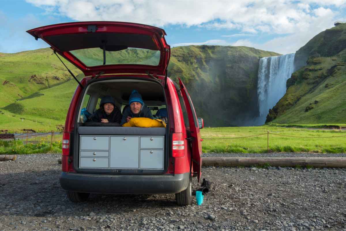 Ventajas y desventajas de alquilar una autocaravana en Islandia Campers tendidos en la cama de su camper con vista de la cascada Skógafoss