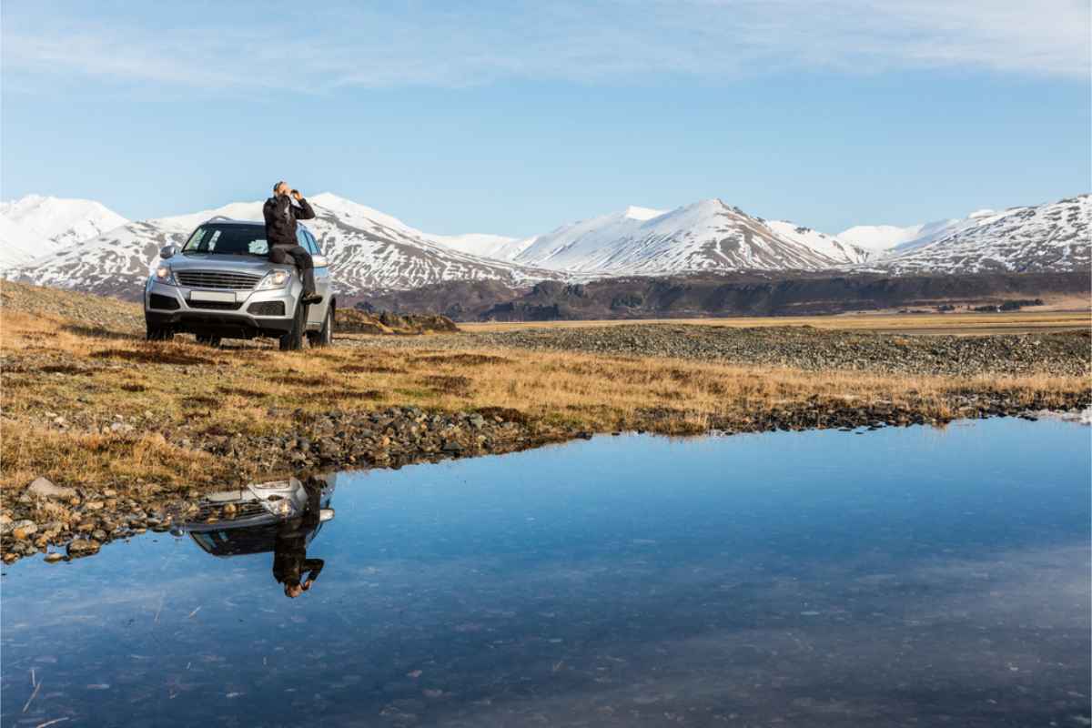 Alquilar un coche en Islandia: los mejores consejos Turista sentado sobre su coche de alquiler contemplando el paisaje islandés