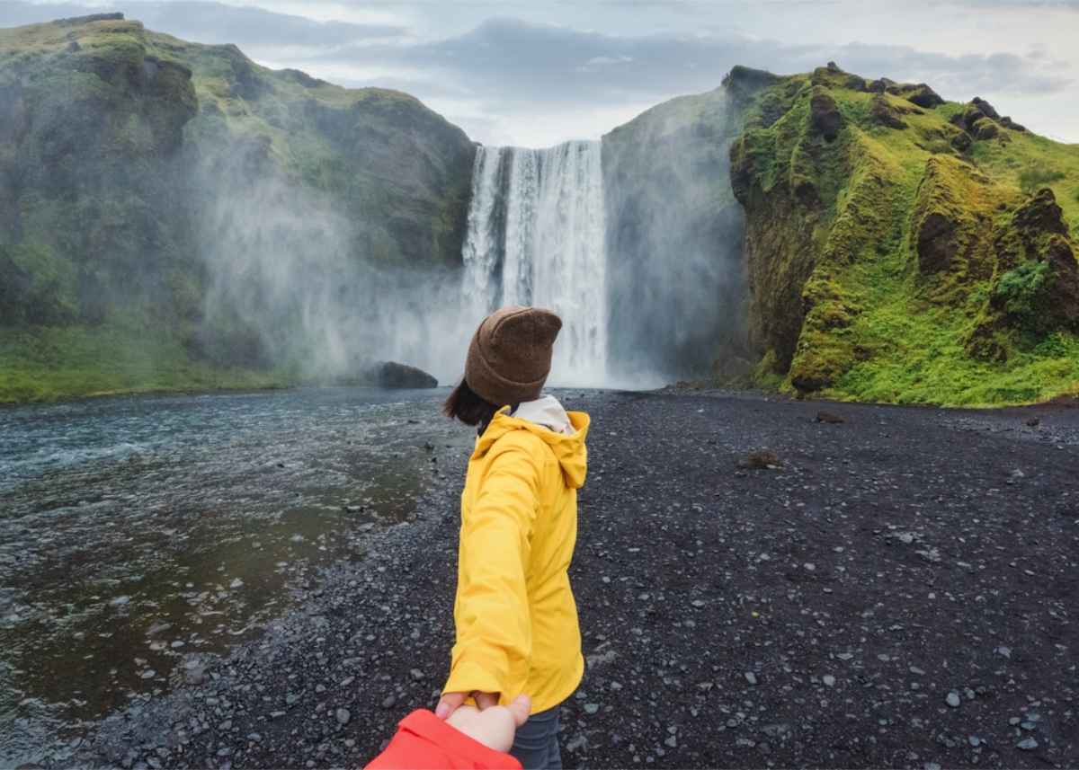 Cascada Skógafoss, sur de Islandia Mujer cogiendo de la mano a su novio en Skogafoss