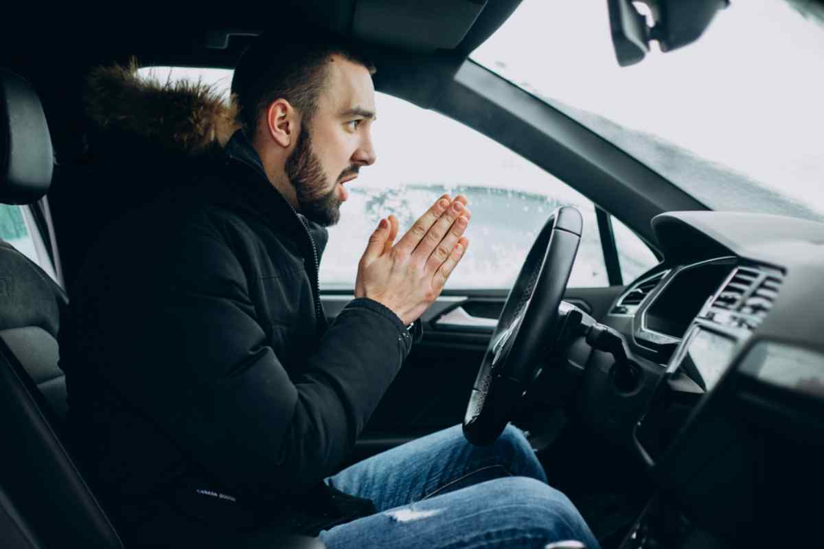 Conductor sentado dentro de un coche frío en invierno, calentándose las manos mientras espera ayuda.