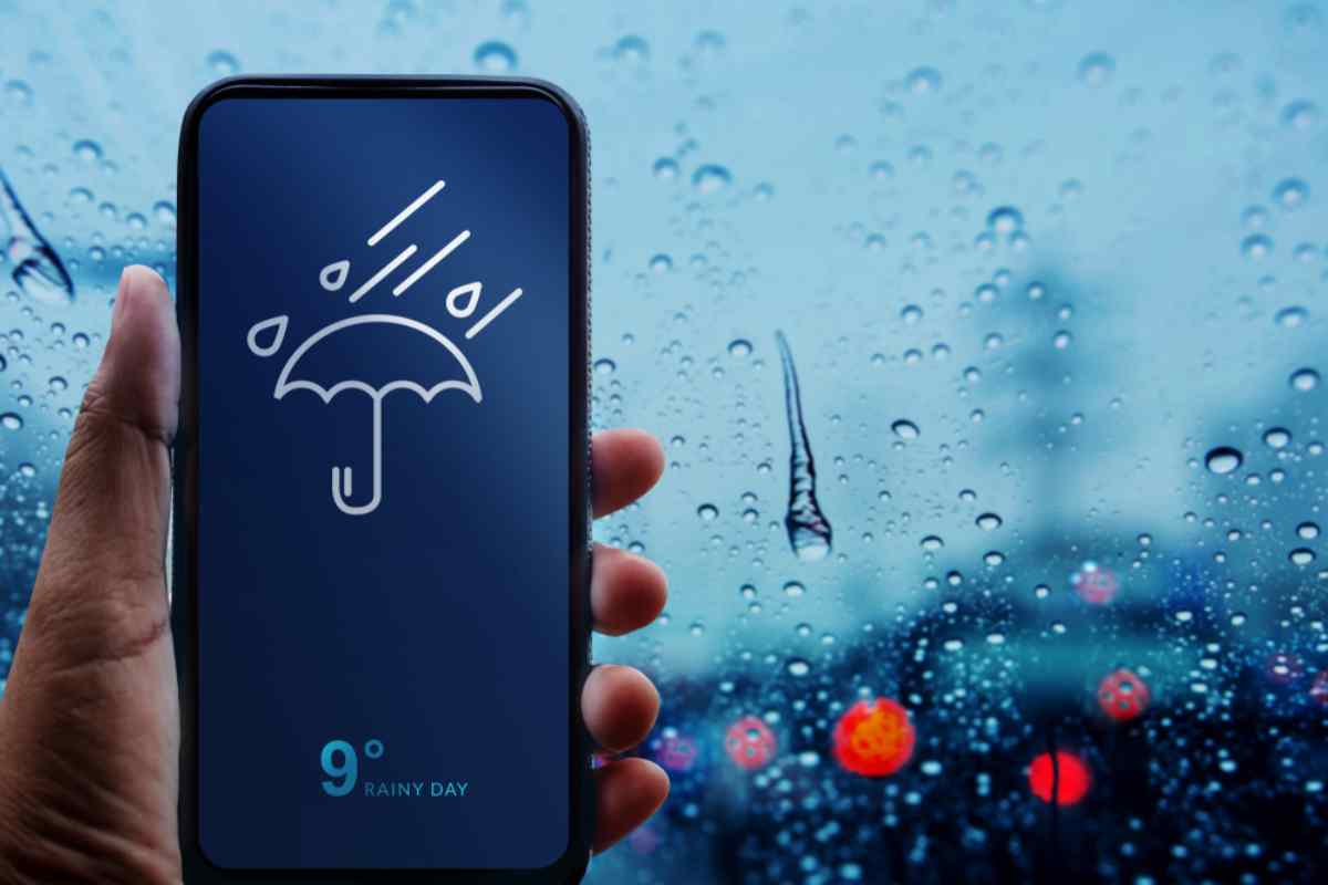 Mano sosteniendo un smartphone que muestra una app del tiempo en un día lluvioso.