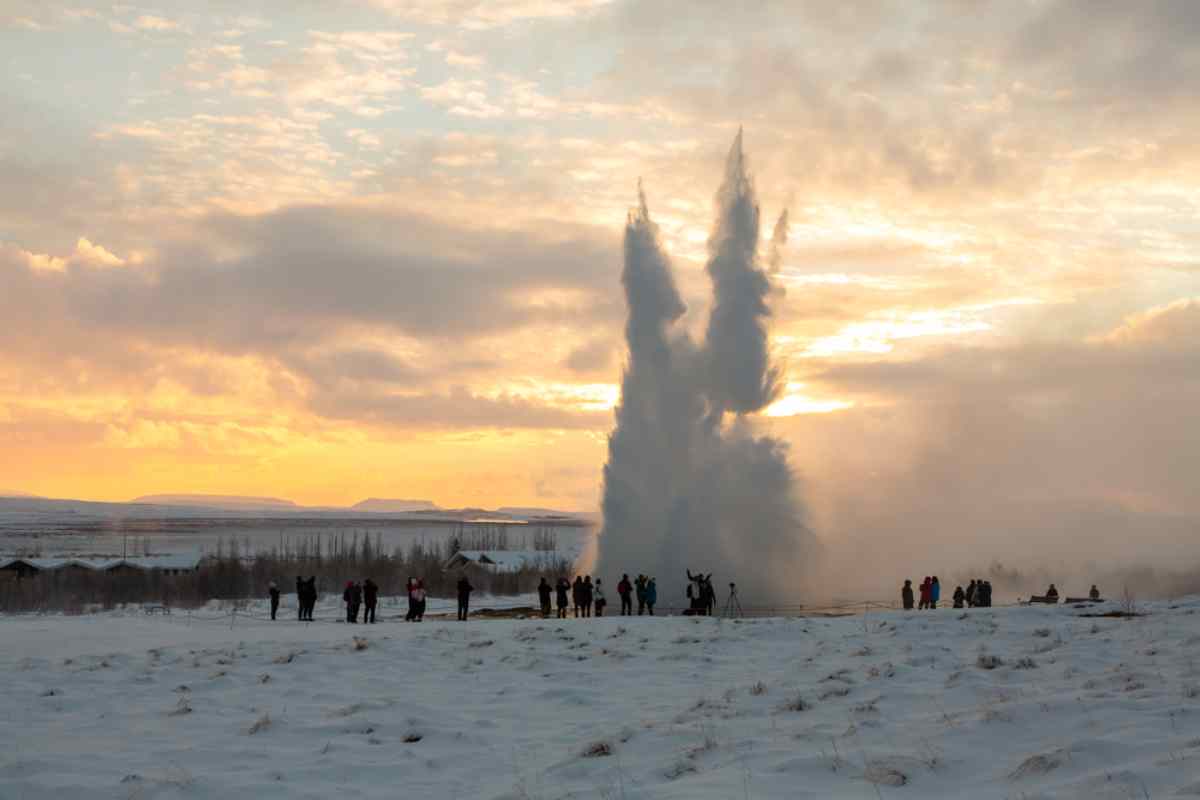 Turistas observando la erupción del géiser Strokkur al atardecer en Islandia durante el invierno.