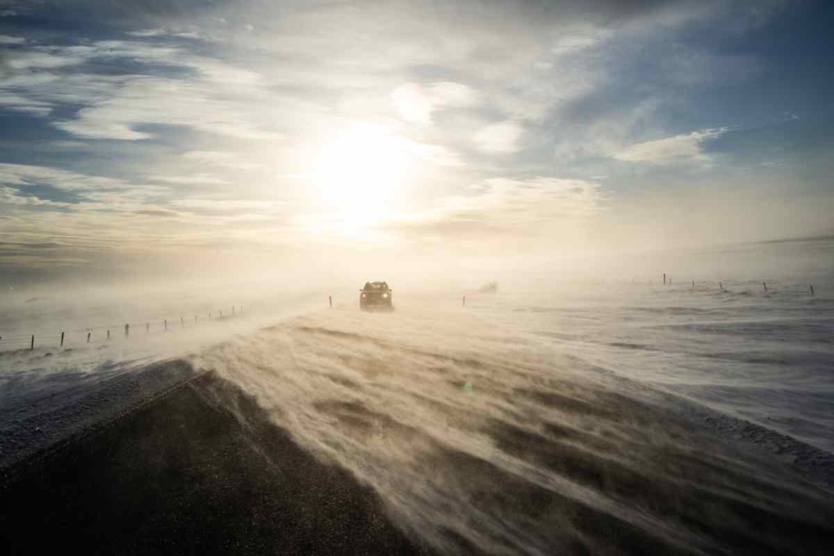 Vehículo conduciendo entre fuerte nieve y viento en una carretera islandesa en invierno.