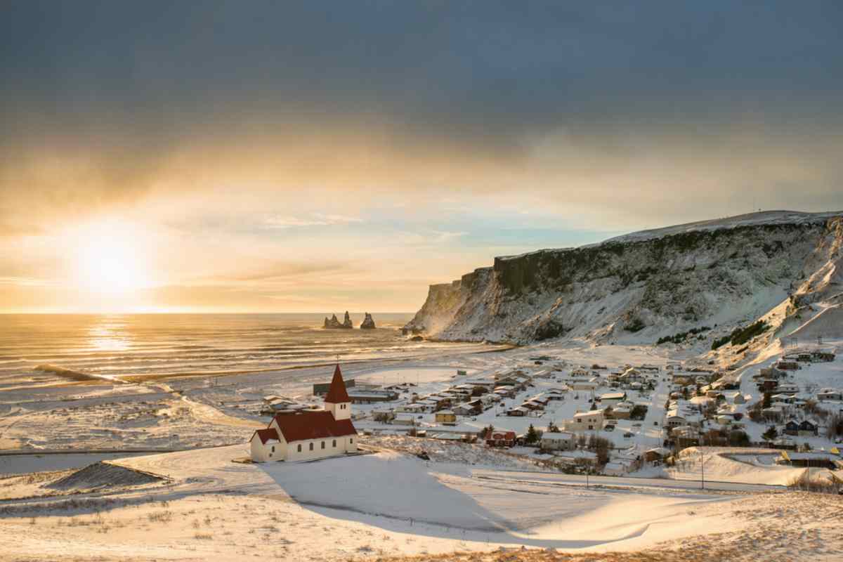 Pueblo de Vík cubierto de nieve en Islandia al amanecer con los pináculos marinos de Reynisdrangar al fondo.