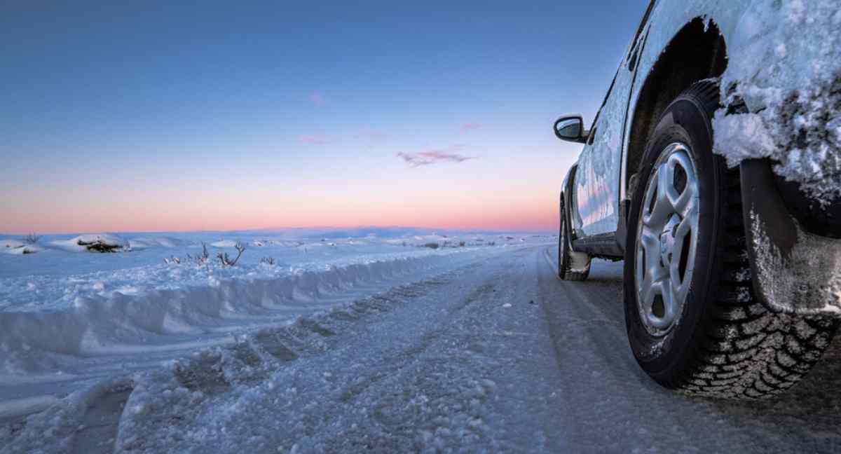 Coche conduciendo por una carretera nevada en Islandia durante una puesta de sol invernal.