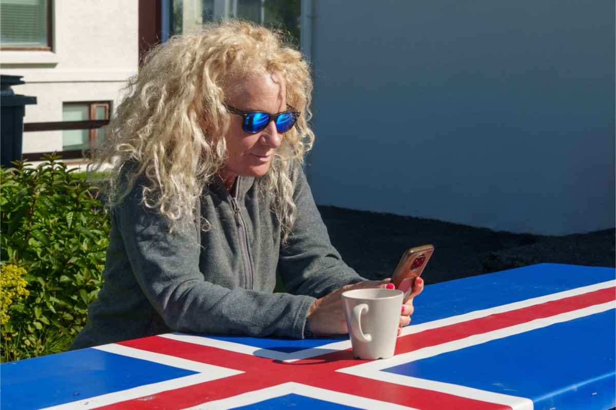 Turista mirando su tel&eacute;fono m&oacute;vil revisando el tiempo sobre una mesa pintada con la bandera de Islandia