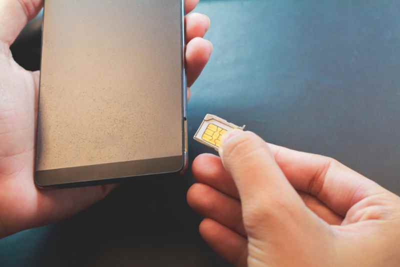 Main ins&eacute;rant une carte SIM dans le plateau d'un smartphone.