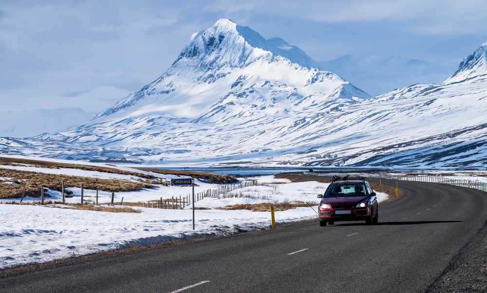 Voiture roulant le long de la Ring Road d&rsquo;Islande avec des montagnes enneig&eacute;es en arri&egrave;re-plan.