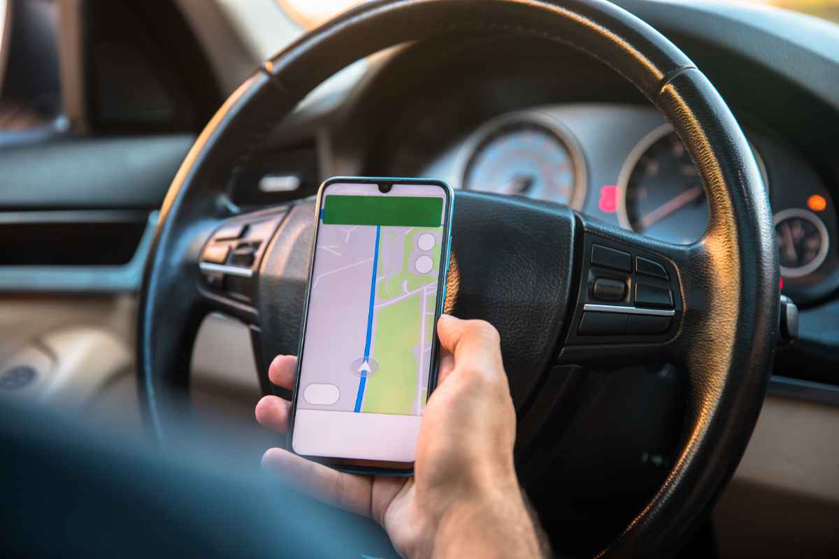 Conducteur Utilisant une Application de Navigation GPS en Conduisant - Guidage d'Itinéraire en Temps Réel Un conducteur tenant un smartphone avec une application de navigation GPS active tout en dirigeant la voiture, montrant un itinéraire sur l'écran du téléphone.