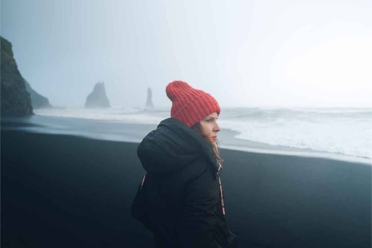 Porter les bons vêtements pour l’Islande Touriste portant la bonne veste en visitant une plage de sable noir en Islande